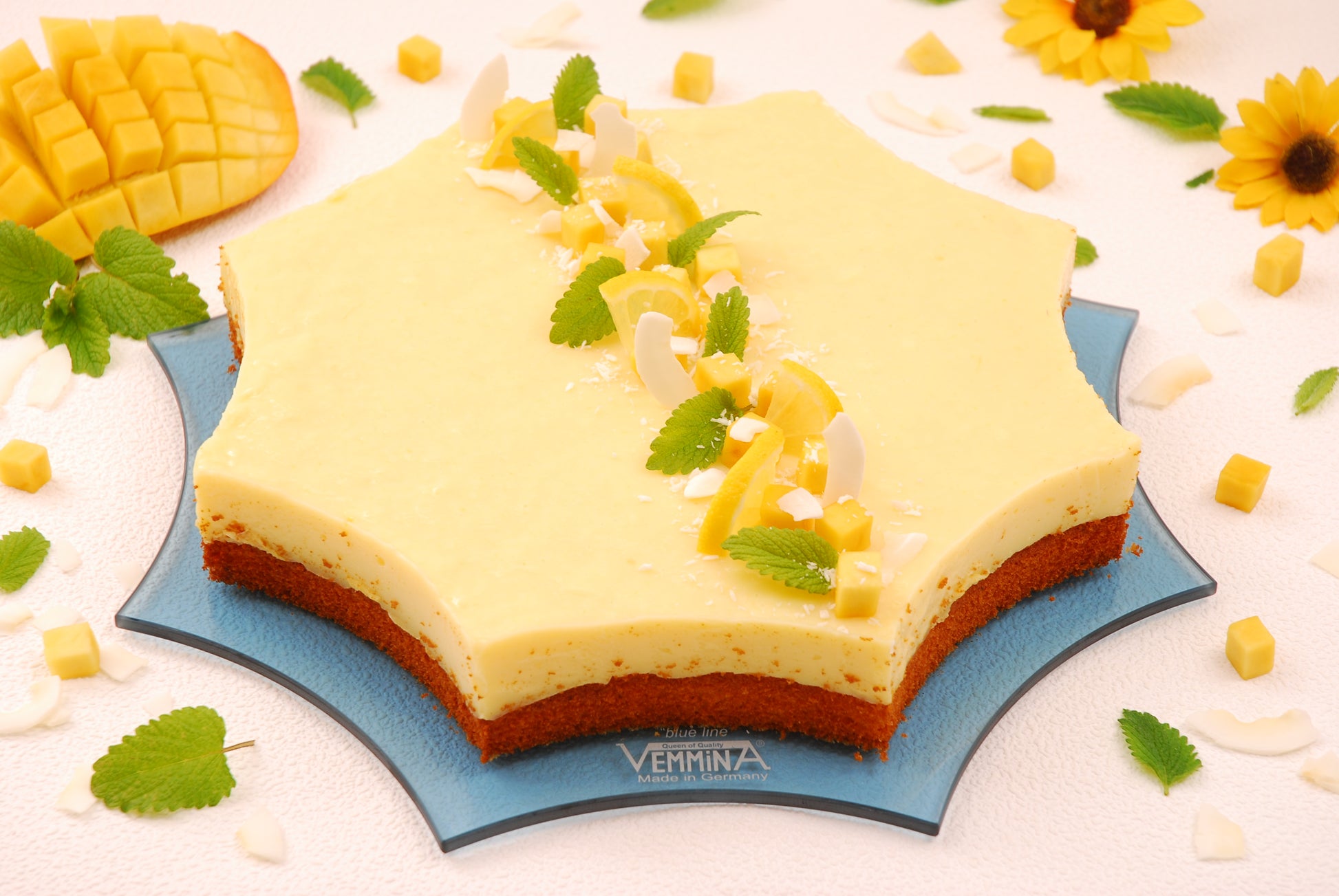 A beautifully decorated star-shaped mango cake topped with mint leaves, coconut, and mango pieces, presented on a blue Cornwall plate.